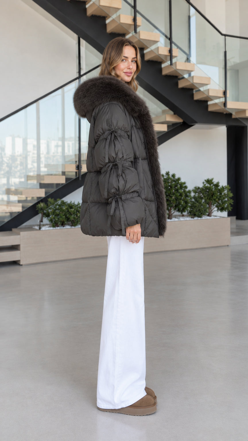 Side profile of women's charcoal quilted puffer coat with faux fur hood and tie sleeves