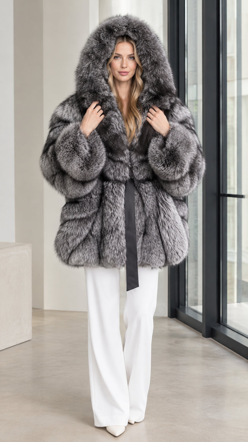 Front full view of a woman wearing a plush silver grey hooded faux fur coat with a black tie belt