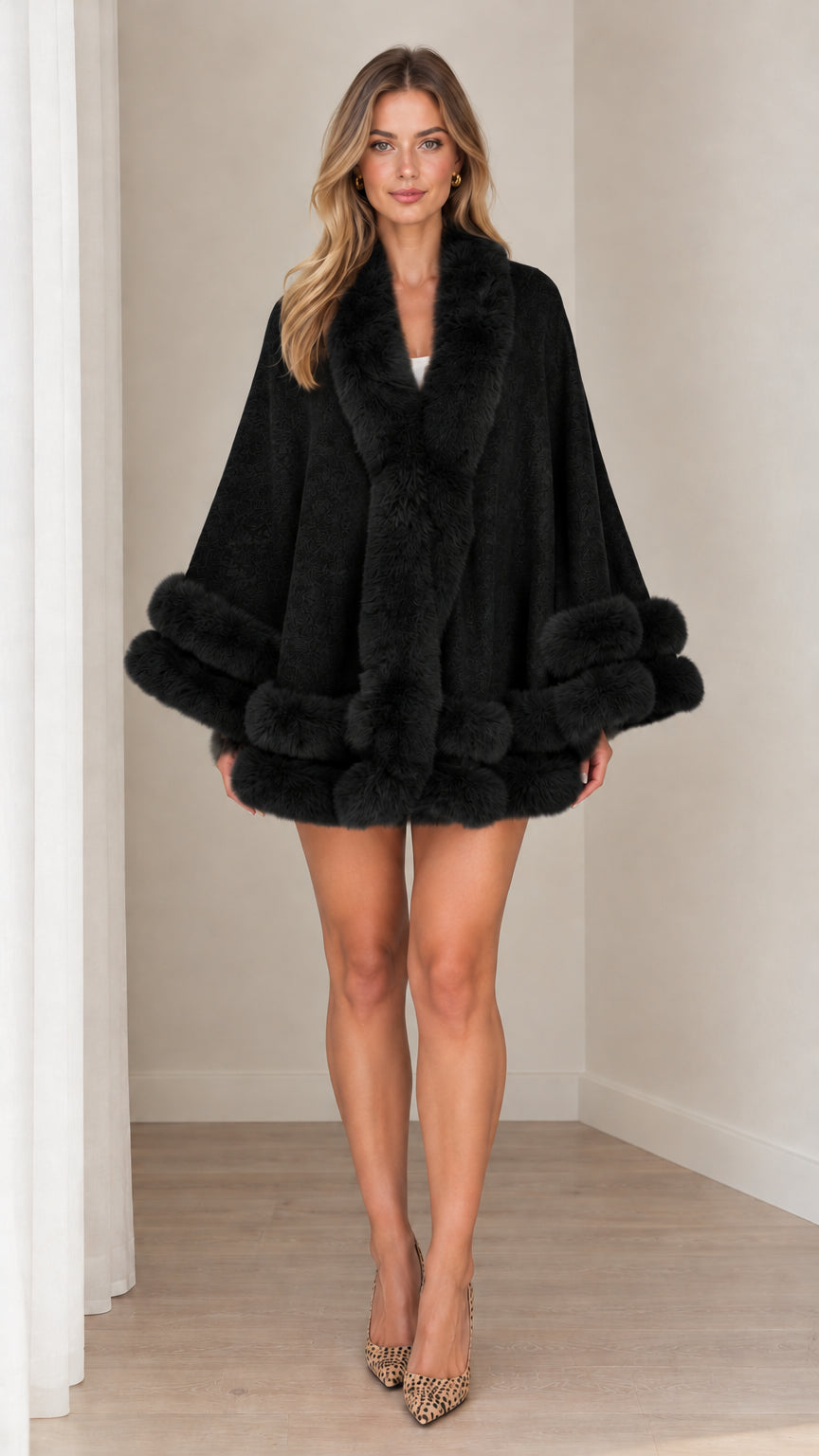 Model wearing black faux fur trim cape coat against neutral studio background